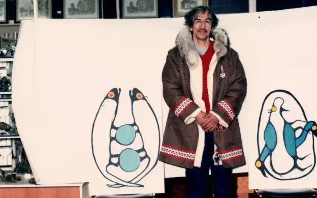 Norval Morrisseau standing next to his paintings
