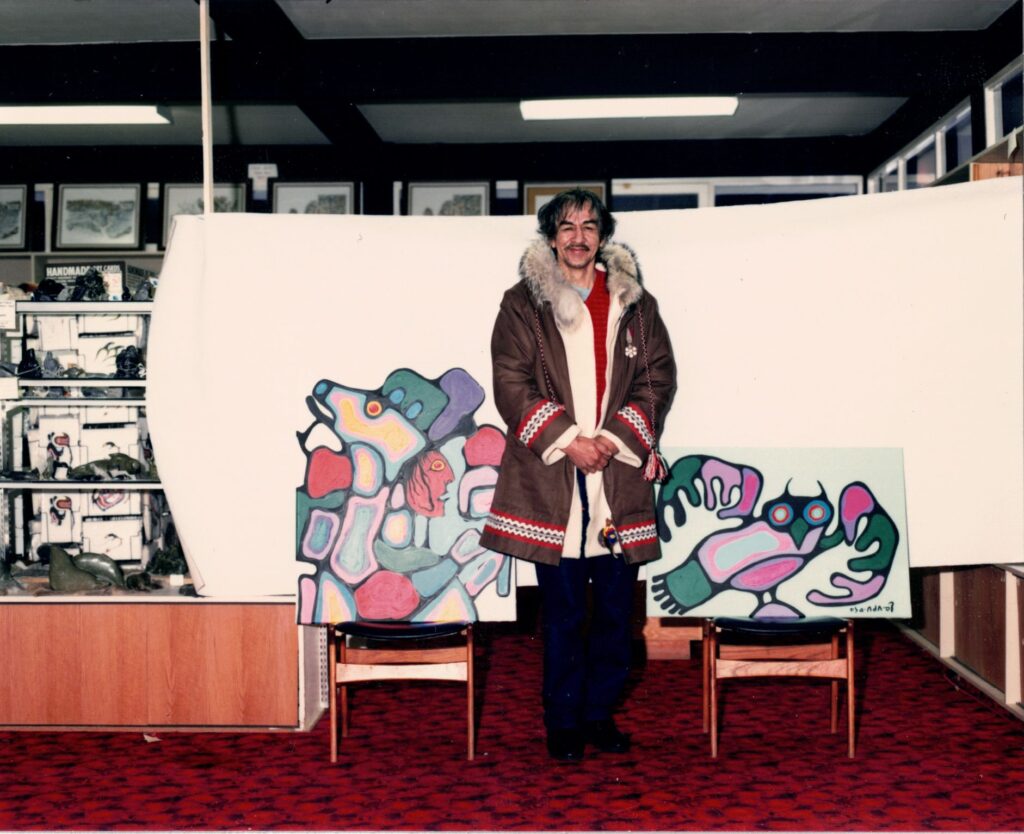 Norval Morrisseau standing in front of a painting